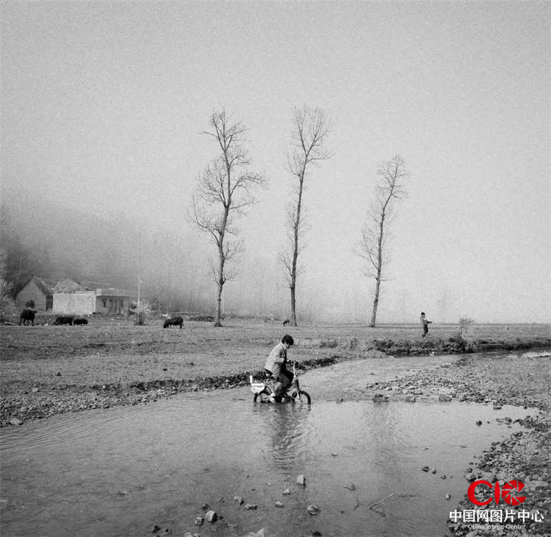 在昭通市的大山包乡，一个孩子正骑着儿童自行车趟过浅河滩。