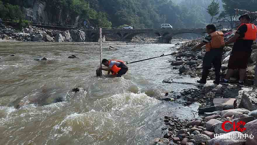 李曉亮在同事的幫助下，繫上安全繩在水流湍急的河道固定測量水尺。