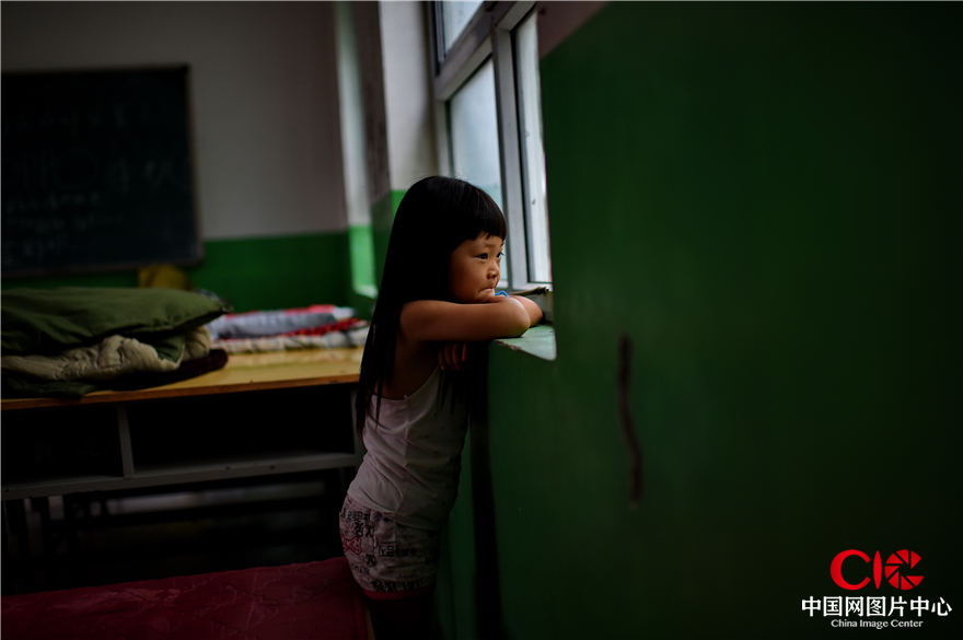 8月3日，磁县南王庄临时安置点，8岁的慧慧透过窗户看着被毁的家园。她说家里的房子坏了、猪没了，就连最喜欢的洋娃娃也被冲走。如今，父母、她和不足10个月的妹妹吃住都在安置点。