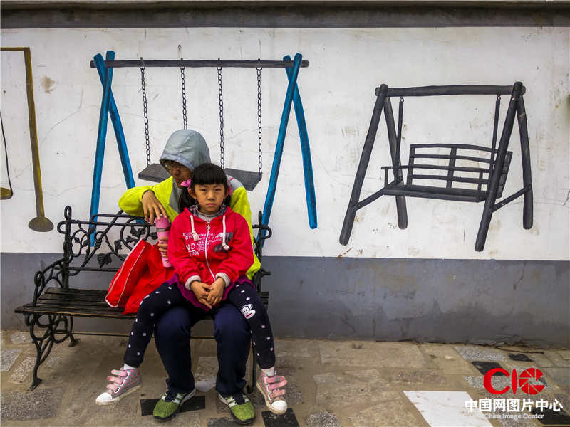 2016.4  河北邯鄲館陶。父女倆坐在墻畫前面的椅子上小憩，真與假的結合，畫面生動有趣兒。