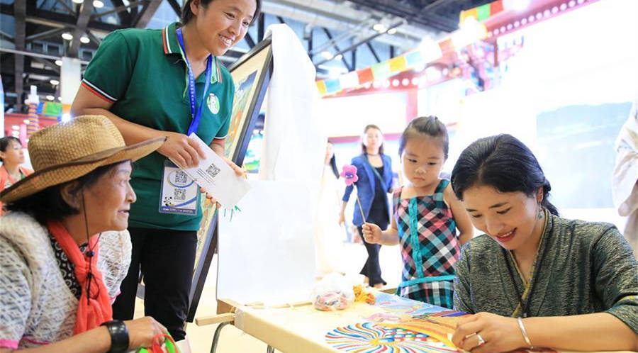 6月17日，青海展区工作人员贡保吉（右）向观众展示藏族刺绣技艺。